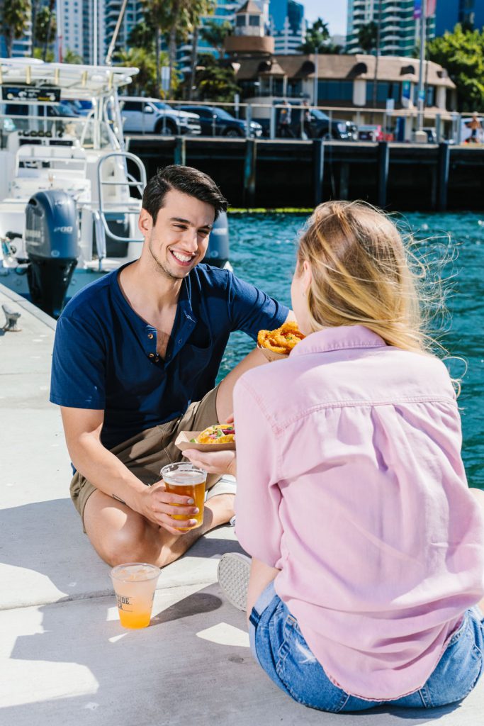 man and woman smiling by the water eating tacos